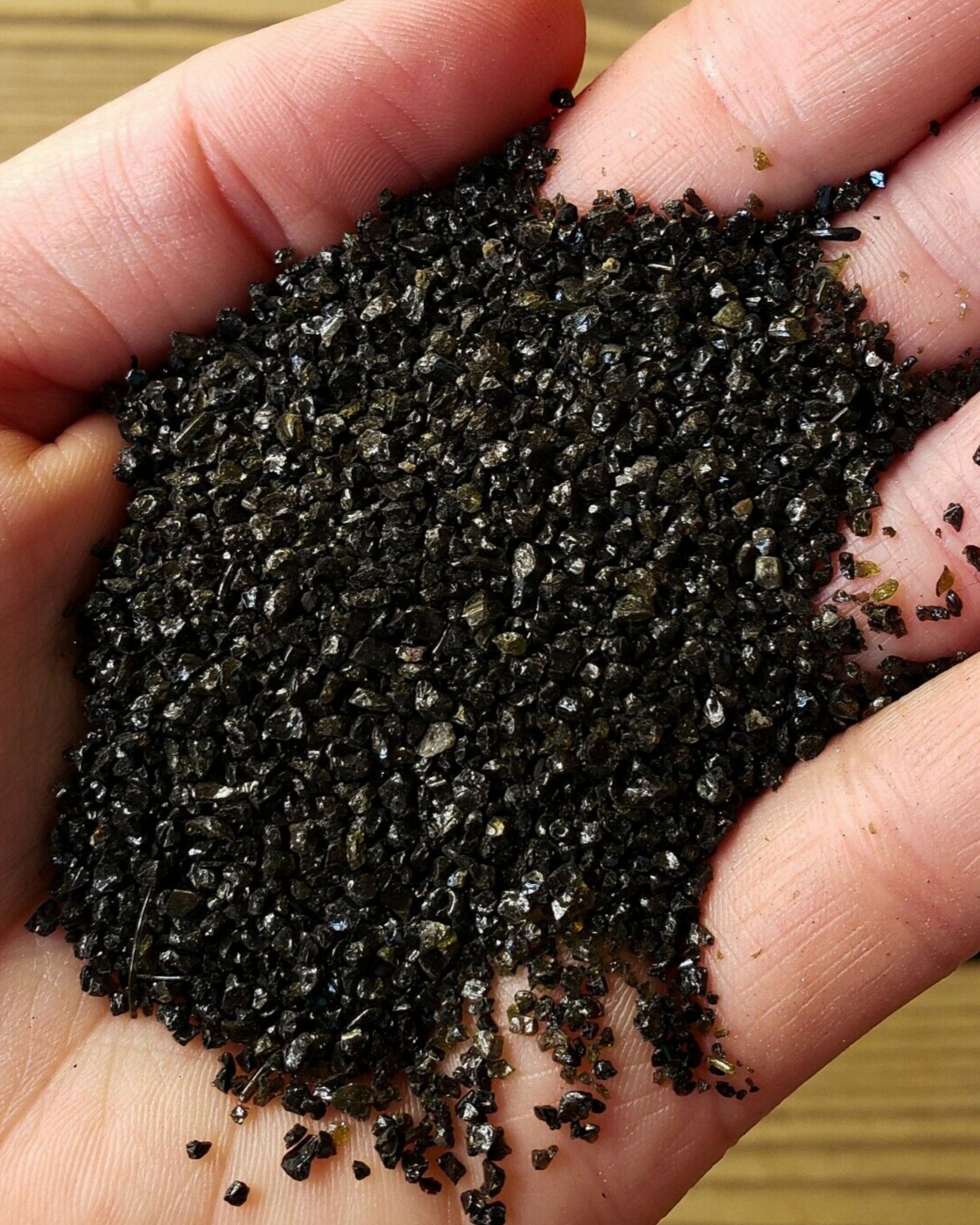 Hand holding a small amount of black sand aquarium substrate